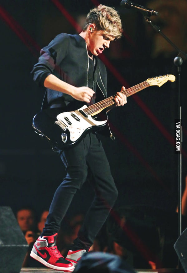 One Direction member fakes playing guitar on stage with a guitar that is not plugged in.